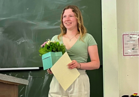 Annika Mahn steht nach der Preisverleihung stolz vor einer Tafel in einem Hörsaal. In ihren Händen hält sie ihre gewonnene Urkunde und einen Blumenstrauß.